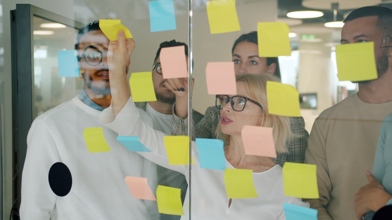 Marketing team brainstorming email campaign ideas together on a glass board with sticky notes